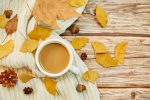 A closeup shot of a cup of coffee and autumn leaves on wooden background